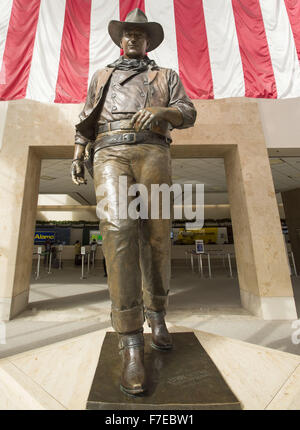 Santa Ana, Kalifornien, USA. 27. November 2015. Eine überlebensgroße Bronzestatue von John Wayne ist auf dem Display an John Wayne International Airport. Wayne, ein Hollywood-Schauspieler berühmt für seine Rollen als harte Cowboys, lebte in Newport Strand. Die Bronzestatue von Wayne wird umrahmt durch eine amerikanische Flagge im Hintergrund hinter zur Veranschaulichung eines Bildes des Patriotismus für eine Generation, die auf seine Filme repräsentieren den heftigen und ikonischen Individualismus viel gehegt und gepflegt von damals in der amerikanischen Geschichte und Kultur aufgewachsen. Wayne ist dargestellt, wie er in den meisten seiner westlichen Filme als robuste Individualist, Hea war, Stockfoto