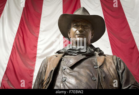 Santa Ana, Kalifornien, USA. 27. November 2015. Eine überlebensgroße Bronzestatue von John Wayne ist auf dem Display an John Wayne International Airport. Wayne, ein Hollywood-Schauspieler berühmt für seine Rollen als harte Cowboys, lebte in Newport Strand. Die Bronzestatue von Wayne wird umrahmt durch eine amerikanische Flagge im Hintergrund hinter zur Veranschaulichung eines Bildes des Patriotismus für eine Generation, die auf seine Filme repräsentieren den heftigen und ikonischen Individualismus viel gehegt und gepflegt von damals in der amerikanischen Geschichte und Kultur aufgewachsen. Wayne ist dargestellt, wie er in den meisten seiner westlichen Filme als robuste Individualist, Hea war, Stockfoto