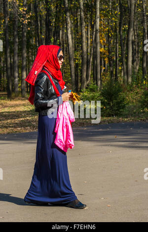 23/09 Frau trägt helle muslimische Kleidung und eine rote Hijab Kopftuch geht in einem Park während der Herbst-Sonne in Ufa-Russland während Stockfoto