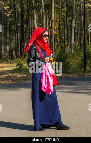 23/09 Frau trägt helle muslimische Kleidung und eine rote Hijab Kopftuch geht in einem Park während der Herbst-Sonne in Ufa-Russland während Stockfoto