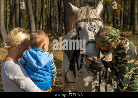 23/09 - Mann in militärische Tarnung Strichen ein weißes Pferd als Frau und junge Baby schauen Sie sich den Ausdruck der Zuneigung in Ufa Ru Stockfoto