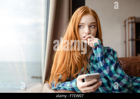 Nachdenklich unconfident rothaarige junge Dame im karierten Hemd, Musik vom Handy hören Stockfoto