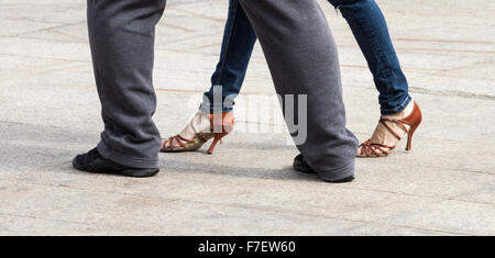 Paare tanzen Tango in Straßencafé in Spanien. Frau trägt Jeans und Heels; Mann in Anzug und Trainer. Stockfoto