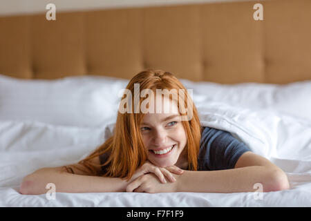 Porträt einer lächelnden rothaarige Frau im Bett liegen und wegsehen Stockfoto