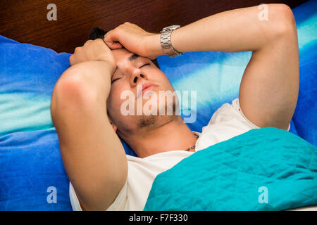 Junger attraktiver Mann halten Kopf und liegen im Bett - schließen sich der kranke Mann mit Kopfschmerzen im Bett erholt Stockfoto