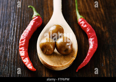 Oliven auf Holzlöffel umgeben von rotem Pfeffer und Knoblauch Stockfoto