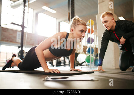 Fitness-Frau mit Fitness-Trainer im Fitness-Studio trainieren. Frau Push Ups Übung mit ihrem persönlichen Trainer im Health Club. Stockfoto