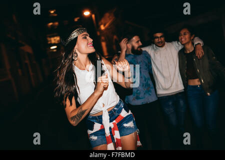Porträt der hübschen jungen Frau tanzt mit ihren Freunden im Hintergrund. Glückliche junge weibliche genießen in einer Party mit Freunden. Stockfoto