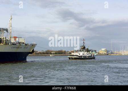 Arbeitsboot Schlepper Führung ein großes Containerschiff durch den schmalen Eingang des Hafens von Portsmouth. Stockfoto