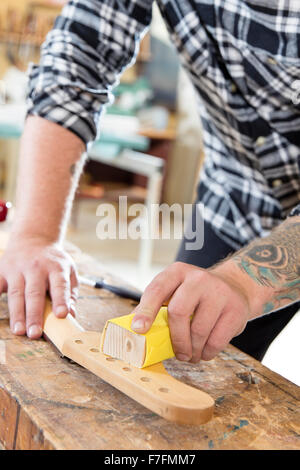 Tischler Schleifen einen Gitarrenhals aus Holz in Werkstatt Stockfoto