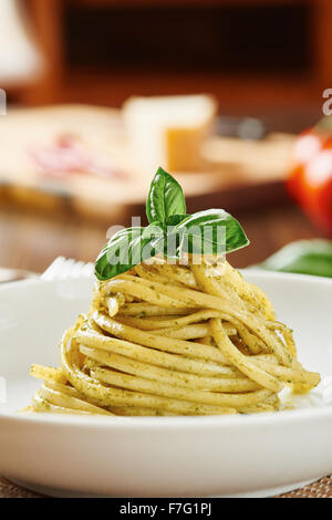 Pasta mit Pesto-Sauce auf weißen Teller umgeben von Zutaten, auf Holztisch Stockfoto