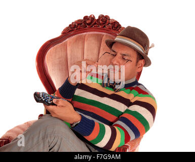 Eine Mitte sind Mann mit Hut in einem rosa Sessel halten seine Brille und die TV-Fernbedienung, isoliert für weiß Stockfoto
