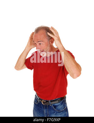 Ein älterer Mann in einem roten T-shirt und Jeans mit seinen Händen auf seinem Kopf schreien für weißen Hintergrund isoliert stehend. Stockfoto