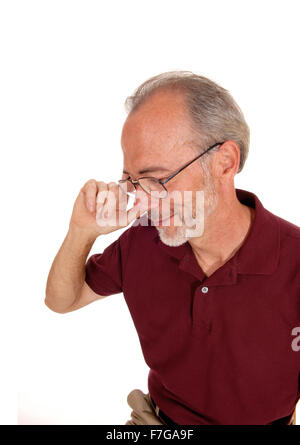 Ein Mann in seinen späteren Jahren sitzt und hält seine Brille in einem Burgunder T-shirt für weißen Hintergrund isoliert. Stockfoto