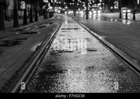 Nacht Blick auf nasse Straßenbahnschienen nach Regen. Verschwommene Ampel auf Hintergrund, schwarz / weiß-Ton Stockfoto