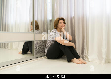 nachdenkliche Frau sitzt in der Ecke des Raumes auf dem Boden Stockfoto