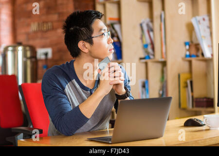 Nachdenklichen jungen asiatischen Mann in Gläsern mit Laptop im café Stockfoto