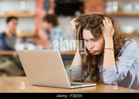 Erschöpft betonte junge Frau mit zerzausten Haaren im Café sitzen und mit laptop Stockfoto
