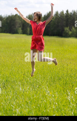 Junges Mädchen in einem roten Kleid an einem sonnigen Tag in einem Feld springen Stockfoto