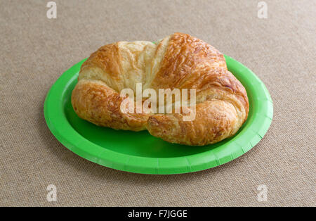 Ein frisch gebackenes Croissant Kruste auf eine grüne Platte oben auf Sackleinen Tischdecke mit natürlichem Licht beleuchtet. Stockfoto