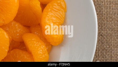 Enge Draufsicht einer Portion Dose Mandarin-Orangen auf einem weißen Teller oben auf einer Tischdecke Sackleinen. Stockfoto