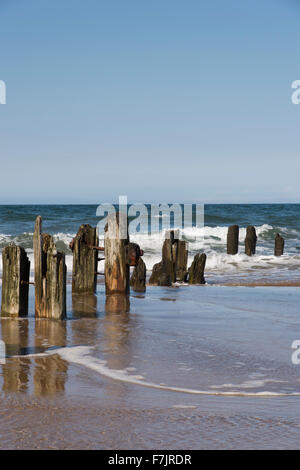 Sonne & blauen Sommerhimmel. Des Meeres Wellen schwappen die Küste, während alte hölzerne Buhnen im Wasser reflektiert werden. Whitbys Strand, Küste von Yorkshire, England, UK. Stockfoto