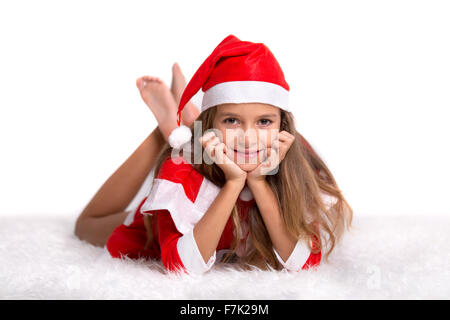 Süßes Mädchen mit einem roten und weißen Weihnachten Santa Hut und Anzug liegen auf einem pelzigen weißen Teppich Stockfoto