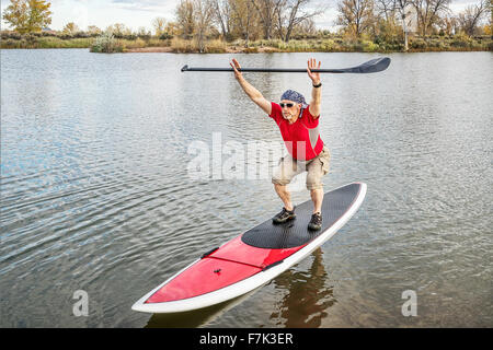 Senior männlichen Paddler dehnen und Aufwärmen auf einem Paddleboard vor paddeln Training auf einem See in Colorado Stockfoto