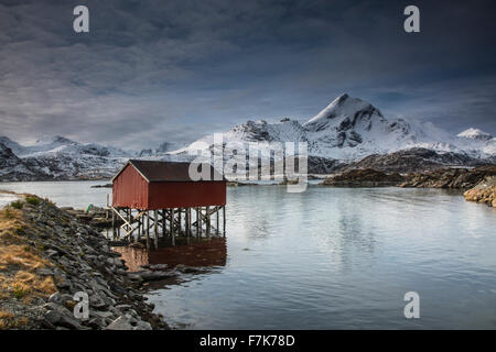 Schneebedeckte Berge hinter Fischerhütte über See, Sund, Lofoten Inseln, Norwegen Stockfoto