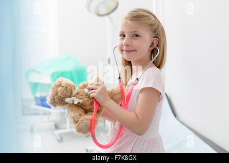 Porträt lächelndes Mädchen mit Stethoskop auf Teddybär im Untersuchungsraum Stockfoto