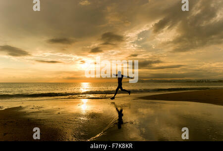 Läufer-Silhouette ist ein Mann dabei, dass einen sportlichen Sprung mit Meer Sonnenuntergang Kulisse entlang des Strandes. Stockfoto