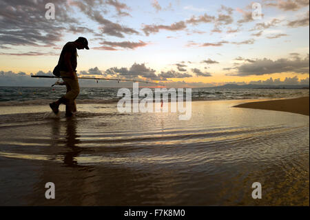 Fischer-Strand ist ein Fischer am Strand entlang spazieren, bei Sonnenaufgang Silhouette gegen den Wolkengebilde Himmel und steigende frühen Mo Stockfoto