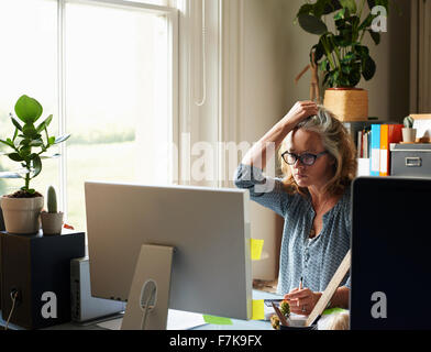 Betonte Frau mit Hand im Haar halten Kreditkarte am Computer im Büro zu Hause Stockfoto