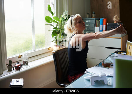 Junge Frau streckte die Arme am Schreibtisch im home-office Stockfoto