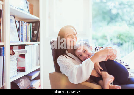 Liebevolle Mutter umarmt Tochter in Sessel Stockfoto