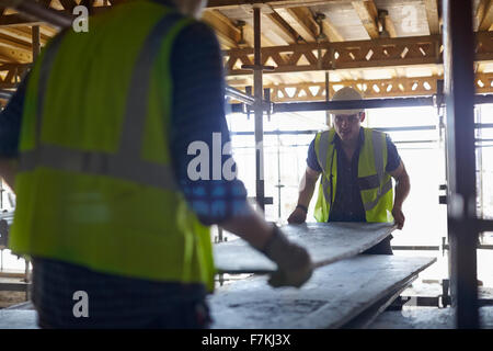 Bauarbeiter, die Aufhebung von Plyboard auf Baustelle Stockfoto