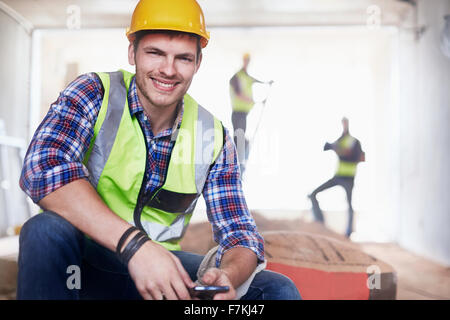 Porträt lächelnd Bauarbeiter mit Handy auf Baustelle Stockfoto