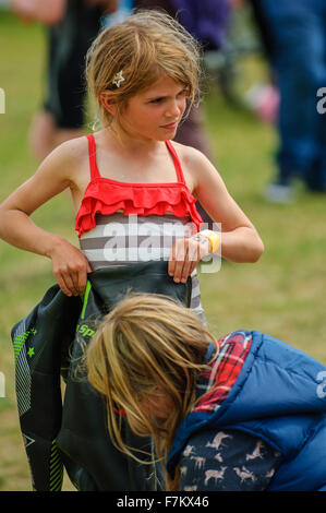 Mama hilft junge blondes Mädchen auf einen Neoprenanzug für einen Triathlon zu setzen Stockfoto