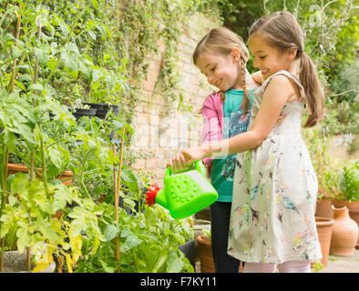 Umarmt Mädchen Bewässerung von Pflanzen im Garten Stockfoto