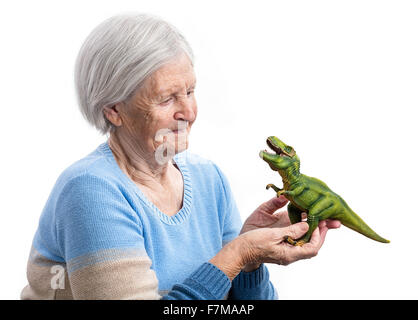 Portrait einer älteren Frau hält einen Spielzeug Dinosaurier über weißem Hintergrund, Aging-Konzept, humorvolle Aspekt Stockfoto