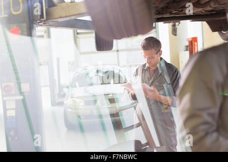 Mechaniker mit Zwischenablage unter Auto in Auto-Werkstatt Stockfoto