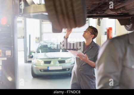 Mechaniker mit Zwischenablage unter Auto in Auto-Werkstatt Stockfoto