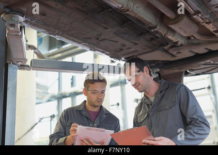 Mechanik mit Klemmbrettern sprechen unter Auto in Auto-Werkstatt Stockfoto