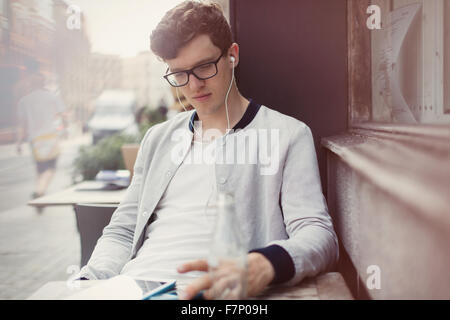 Junger Mann mit Brille und Kopfhörer mit digital-Tablette am Straßencafé Stockfoto