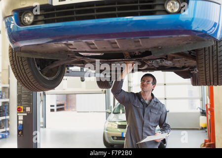 Mechaniker mit Zwischenablage funktioniert unter Auto in Auto-Werkstatt Stockfoto