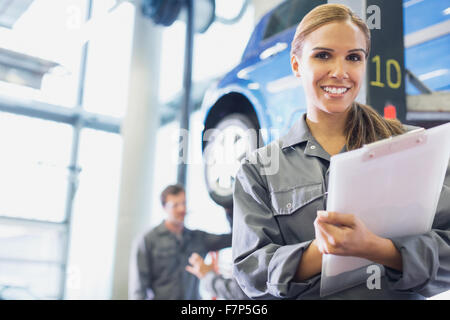 Porträt lächelnd Mechaniker mit Zwischenablage in Autowerkstatt Stockfoto
