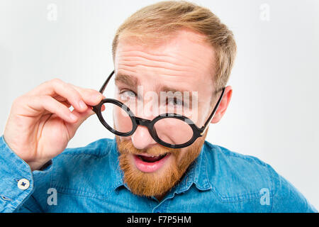 Amüsante glücklich fröhliche junge Mann mit Bart mit Blick auf seine Runde Brille isoliert auf weißem Hintergrund Stockfoto