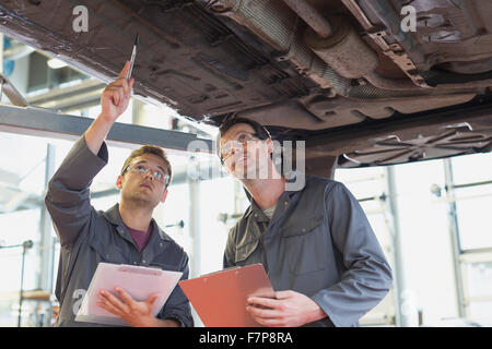 Mechanik mit Klemmbrettern unter Mietwagen in Autowerkstatt Stockfoto