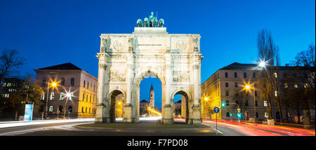 Das Siegestor (Englisch: Triumphbogen) in München. Dies ist eine lange Belichtung in der Abenddämmerung mit Datenverkehr rund um den Bogen Stockfoto