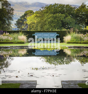 Eine Bank spiegelt sich in das Stille Wasser von einem Seerosenteich auf der Lily Terrace im Bodnant Garden, Conwy, Wales, im Oktober. Stockfoto